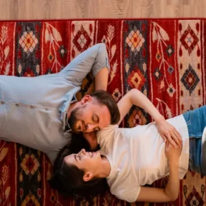 Un couple allongé sur un tapis dans un salon, partageant un moment de détente et d'intimité.