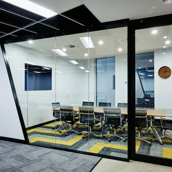 A modern conference room featuring glass walls and several chairs arranged around a central table.