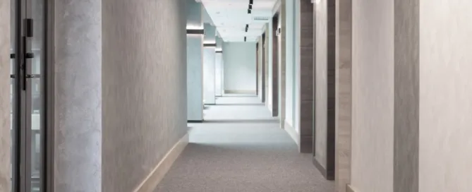 A long hallway featuring gray carpeting, white walls, and a decorative runner rug along the floor.