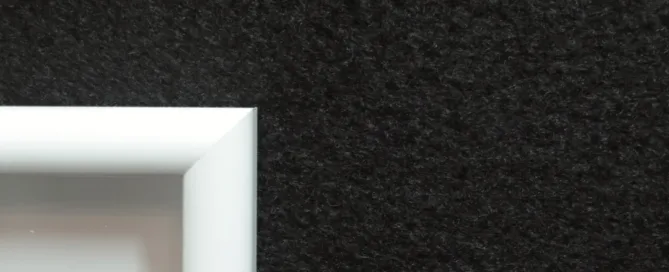 A white square frame mounted on a black wall, which features a textured wall carpet.