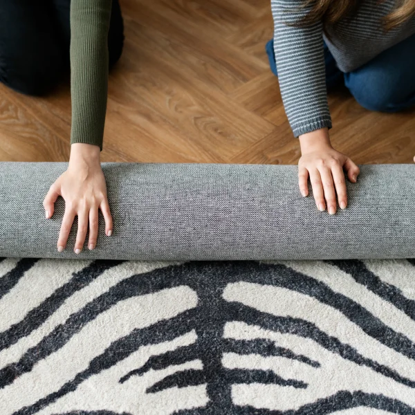 Deux personnes installant un tapis à motif géométrique moderne sur un sol en bois, mettant en valeur le motif et la texture.